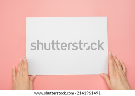 Mockup image. White paper with woman hands on pink background. Woman hands with mockup empty paper sheet on pink background. Hands holding blank advertising card