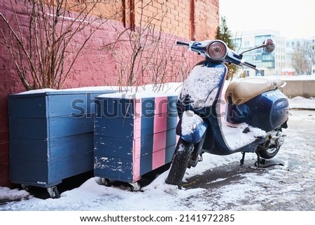 a lone abandoned old rare moped covered in a layer of snow. moped in winter city near red brick wall Royalty-Free Stock Photo #2141972285