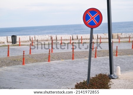 Road sign with prohibition no stop and parking at the turn of the paved road against the backdrop of the sea