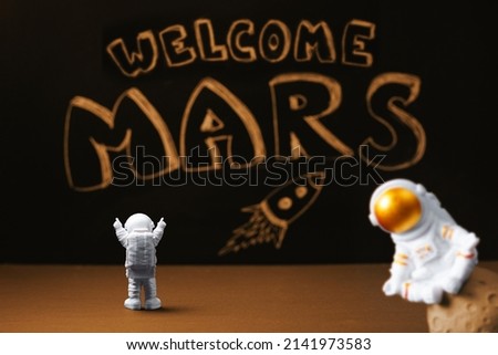 Figures of astronauts on the background of a chalky black board with the inscription welcome to Mars and a flying rocket. Mars colonization.