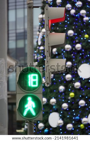 Pedestrian traffic light is green against the background of the Christmas tree