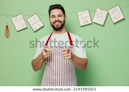 Young smiling male chef confectioner baker man 20s in striped apron point index finger camera on you say do it isolated on plain pastel light green background studio portrait. Cooking food concept.