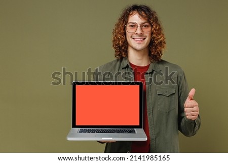 Young brunet curly man 20s wears khaki shirt hold use work on laptop pc computer with blank screen workspace area showing thumb up like gesture isolated on plain olive green background studio portrait