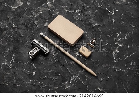 Photo of blank vintage business cards, pencil, eraser and clips on black plaster background. Blank kraft stationery.