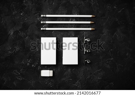 Blank business cards, pencils, eraser and clips on black plaster background. Template for graphic designers portfolios. Top view. Flat lay.