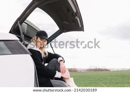 Young girl driver in yellow summer dress and straw hat standing near a car enjoying warm summer day at sunset. Travel and vacation concept.