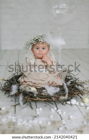 an adorable thoughtful cute little toddler girl in wreath and natural cotton dress is sitting in a nest with feathers? eggs around. Easter concept. relations with parents