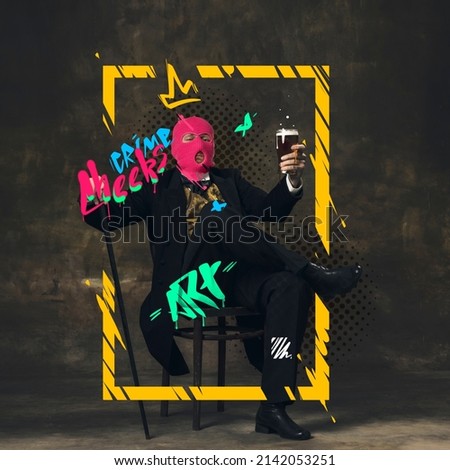 Contemporary artwork. Aristocrat man in pink balaclava sitting on chair and rising class of beer isolated over dark vintage background. Concept of combination of eras, modernity and past. Street style Royalty-Free Stock Photo #2142053251