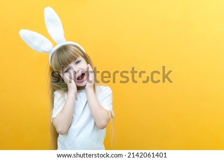 cheerful girl with rabbit ears on her head on a yellow background. Funny crazy happy child. hands a rabbit. Preparation for the Easter holiday. copy space for text, mockup