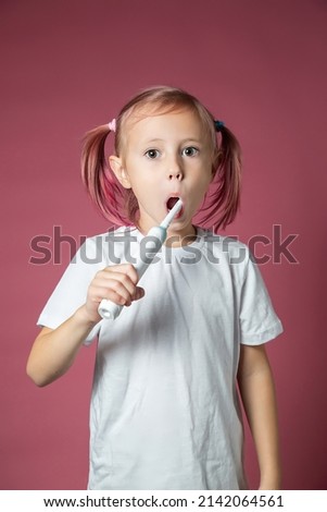 Smiling caucasian little girl cleaning his teeth with electric sonic toothbrush on pink background.