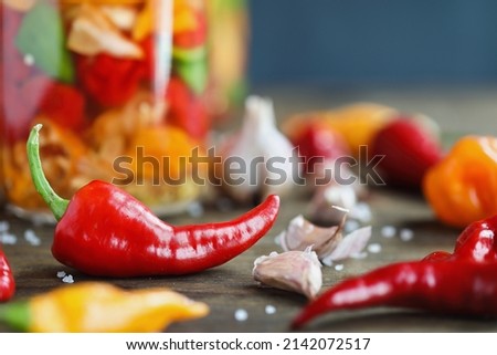 Cyklon pepper with variety of other spicy peppers and garlic cloves in front of a mason jar of fermenting hot sauce. Selective focus with blurred background and foreground.