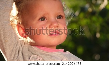 The sun illuminates the face of a small child, she looks up. Surprised look of a little girl.