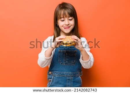Adorable little girl with her tongue out and craving a cheeseburger she is about to eat in a studio