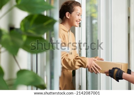 Happy excited young woman receiving package that delivery man brought to her house Royalty-Free Stock Photo #2142087001