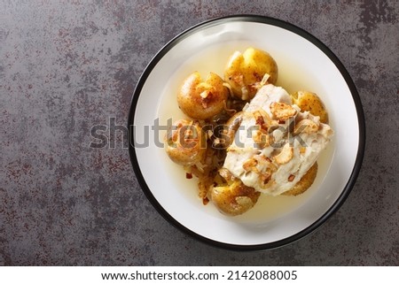 Cod fillet baked in olive oil with garlic served with potatoes close-up in a plate on the table. horizontal top view from above
