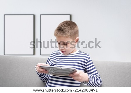 The boy is sitting on the couch with a tablet in his hands