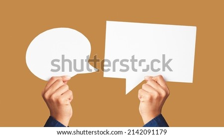 Close-up of hands holding white speech bubbles against a light brown background in the studio. Close-up photo. Space for text