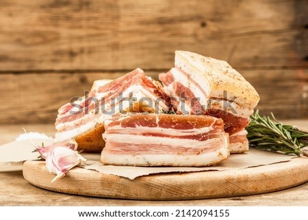 Pieces of salty high-fat meat cooked with spices. Salo, bacon, lard, silverside, gammon. Garlic, fresh rosemary, spices. Hard light, dark shadow, wooden background, copy space Royalty-Free Stock Photo #2142094155