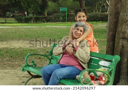 Mid aged mom and daughter sitting outdoors in lush green park in a serene environment. They both are happily enjoying the surroundings and ambience. Happy smile all around. She is enjoying motherhood.