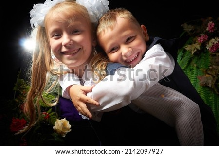 Girl and boy who is elementary school children in uniform having fun on black background with flowers. Brother and sister on September 1 in Russia. Schoolgirl and schoolboy relaxing. Photo shoot