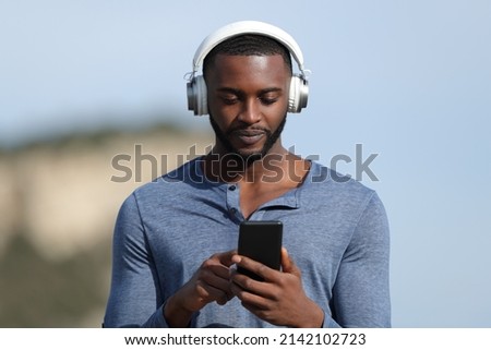 Man with black skin wearing headset listening to music checking smart phone outdoors