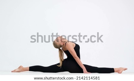A tall, young, Scandinavian woman with long hair wearing a black top and black panties demonstrating a yoga pose