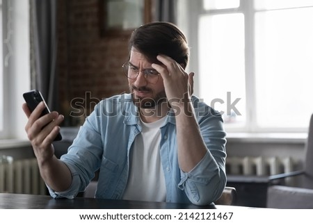 Concerned annoyed smartphone user man staring at cellphone screen with upset face, having problems with online app, banking service, getting bad news, feeling stress about poor connection Royalty-Free Stock Photo #2142121467