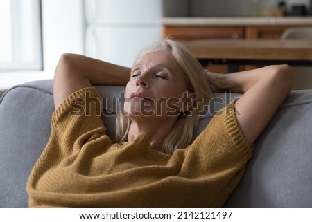 Peaceful sleepy middle aged woman resting on sofa with closed eyes, falling asleep, enjoying break, silent leisure time at home, taking deep breath of fresh air, reducing stress