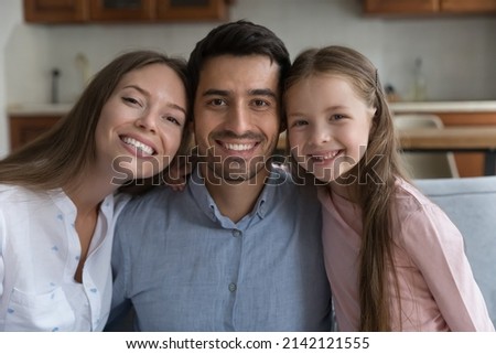 Happy young couple of parents and sweet daughter child head shot portrait. Mom, dad, kid hugging, relaxing together at home, looking at camera with toothy smiles. Parenthood concept Royalty-Free Stock Photo #2142121555