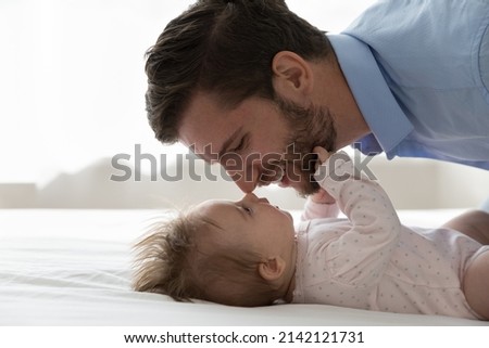 Happy handsome young dad calming, comforting baby resting on back in bed, kissing kid forehead with nose touches, expressing love, tenderness, care, caressing sleepy child. Fatherhood concept Royalty-Free Stock Photo #2142121731