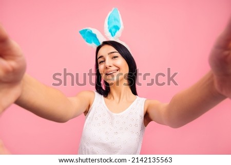 beautiful cheerful woman in rabbit ears makes a selfie, video call, easter, in the studio on a pink background. High quality photo