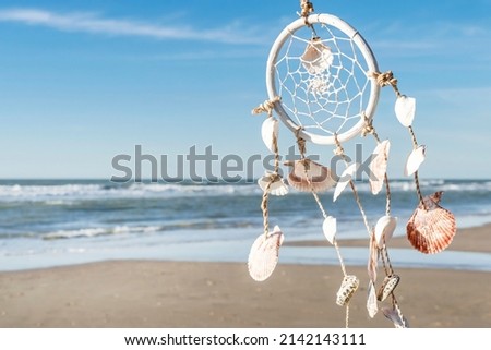 Romantic summer background in hippie style, free space for text. Dreamcatcher in boho style on the background of the sea beach and blue sky.  Royalty-Free Stock Photo #2142143111