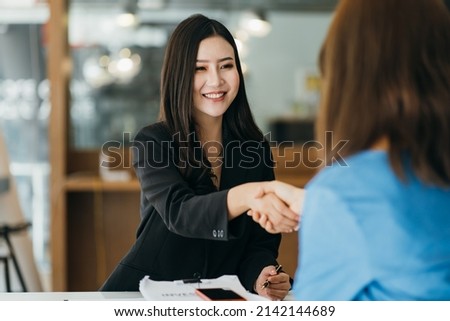 Two Businesswomen Shaking Hands In Modern Office Royalty-Free Stock Photo #2142144689