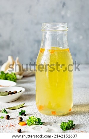 Homemade chicken (bone) broth (bouillon) with vegetables, spices and herbs in a glass bottle on a light background. Natural collagen of animal origin. Liquid broth from meat, fish, vegetables.