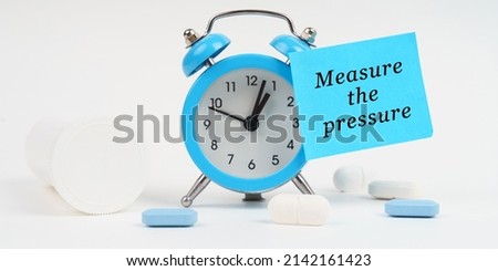 Medical concept. On a white surface there are pills and an alarm clock, on which there is a sticker with the inscription - Measure the pressure