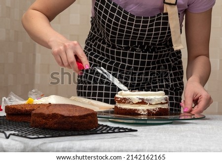 Woman's hand with kitchen spatula smoothes the filling in the cake. Selective focus. Picture for articles about food, confectioners.