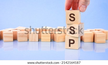 hand holding wood cube block with SSP text. the inscription on the cubes is reflected from the surface. blue background with copy space. SSP - short for Sell Side Platform
