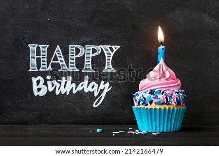 Birthday cupcake with birthday candle in front of chalkboard with happy birthday message