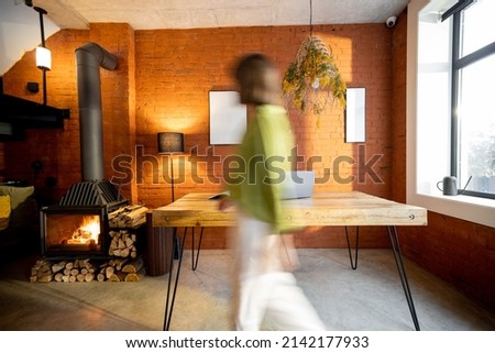 Living room interior in loft style with wooden table and burning fireplace at home. Motion blurred person passing by