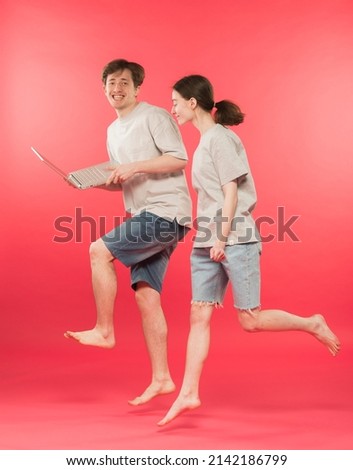 joyful couple guy and girl novice businessmen with a laptop in their hands are moving towards the dream goal on a pink background in the studio