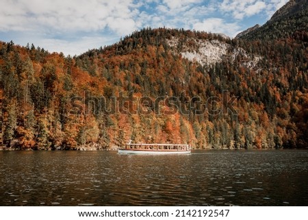View from the lake Konigssee towards to boat with colorful autumn forest and mountains in the background. Berchtesdagen region, Germany.