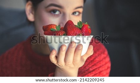 A young woman holds a bowl of strawberries in her hands.