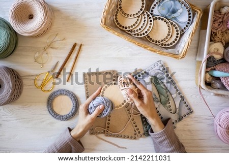 Top view woman hands knitted accessory interior decor use ribbon yarn and wooden stencil pattern on desk table at home. Closeup female arms creating exclusive handmade craft details art work Royalty-Free Stock Photo #2142211031