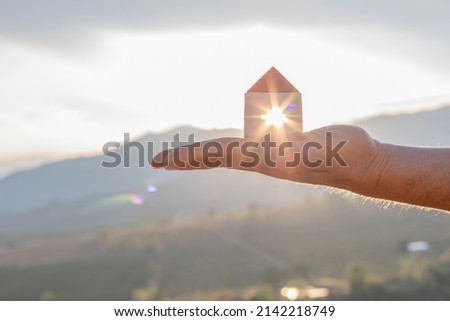 House in hand nature sunset background. protection or property concept.