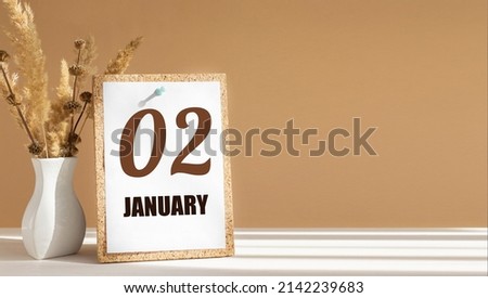 january 2. 2th day of month, calendar date.White vase with dead wood next to cork board with numbers. White-beige background with striped shadow. Concept of day of year, time planner, winter month.