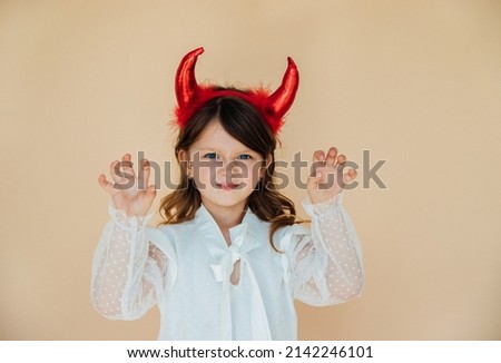 Portrait of a little girl in a white dress with devil horns. Halloween costume. Angry mood. A menacing expression on his face.