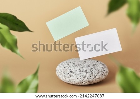 White and green paper business card mockup levitate on pebble stone in blurred leaves frame