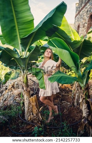 Attractive young fair-skinned woman stands near banana trees in tropical park. Selective focus