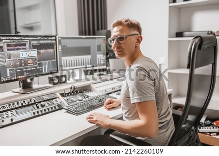 Man working in music studio using computer wearing glasses. Sound engineer working and mixing track. Programmer watching at display of it while listening music. Technology concept