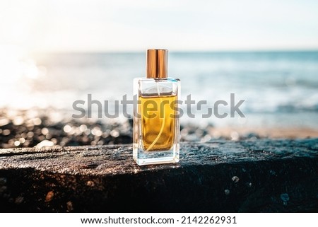 Glass bottle of golden perfume on a wet stone. The oceans surf is in the background. Copy space.